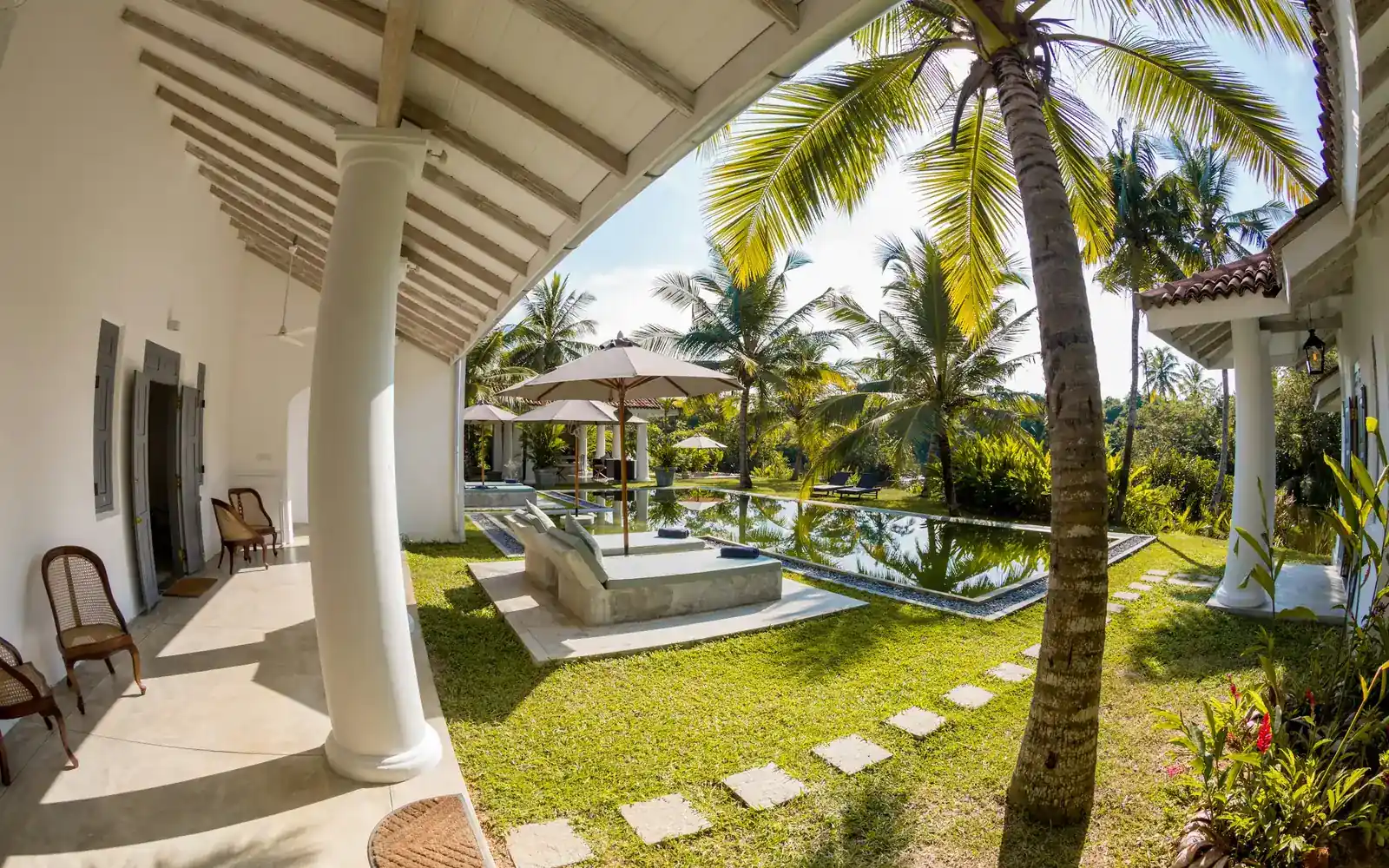 Une véranda de villa donnant sur un jardin de palmiers et une piscine