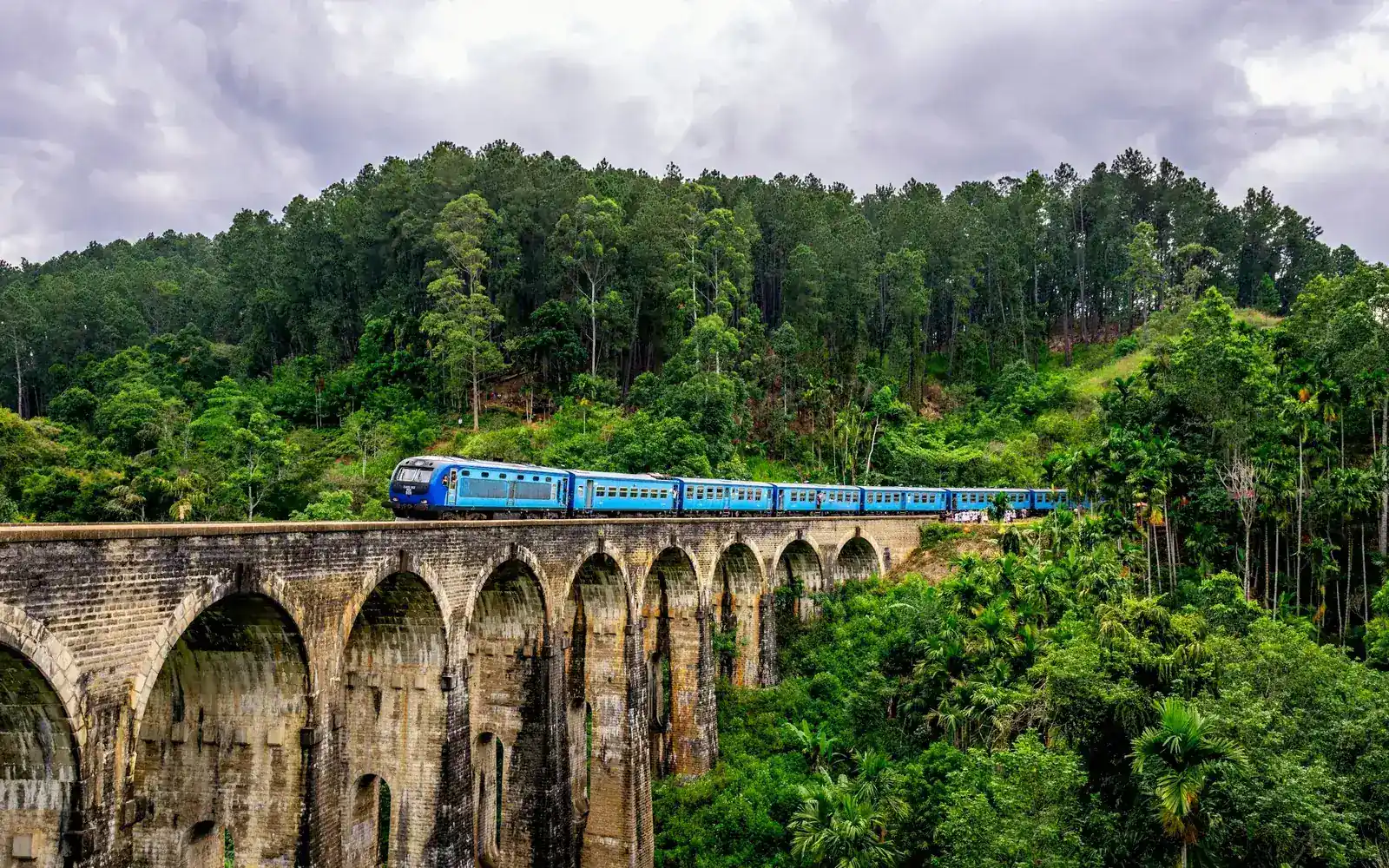 Un train bleu traversant un viaduc de pierre entre des collines vertes